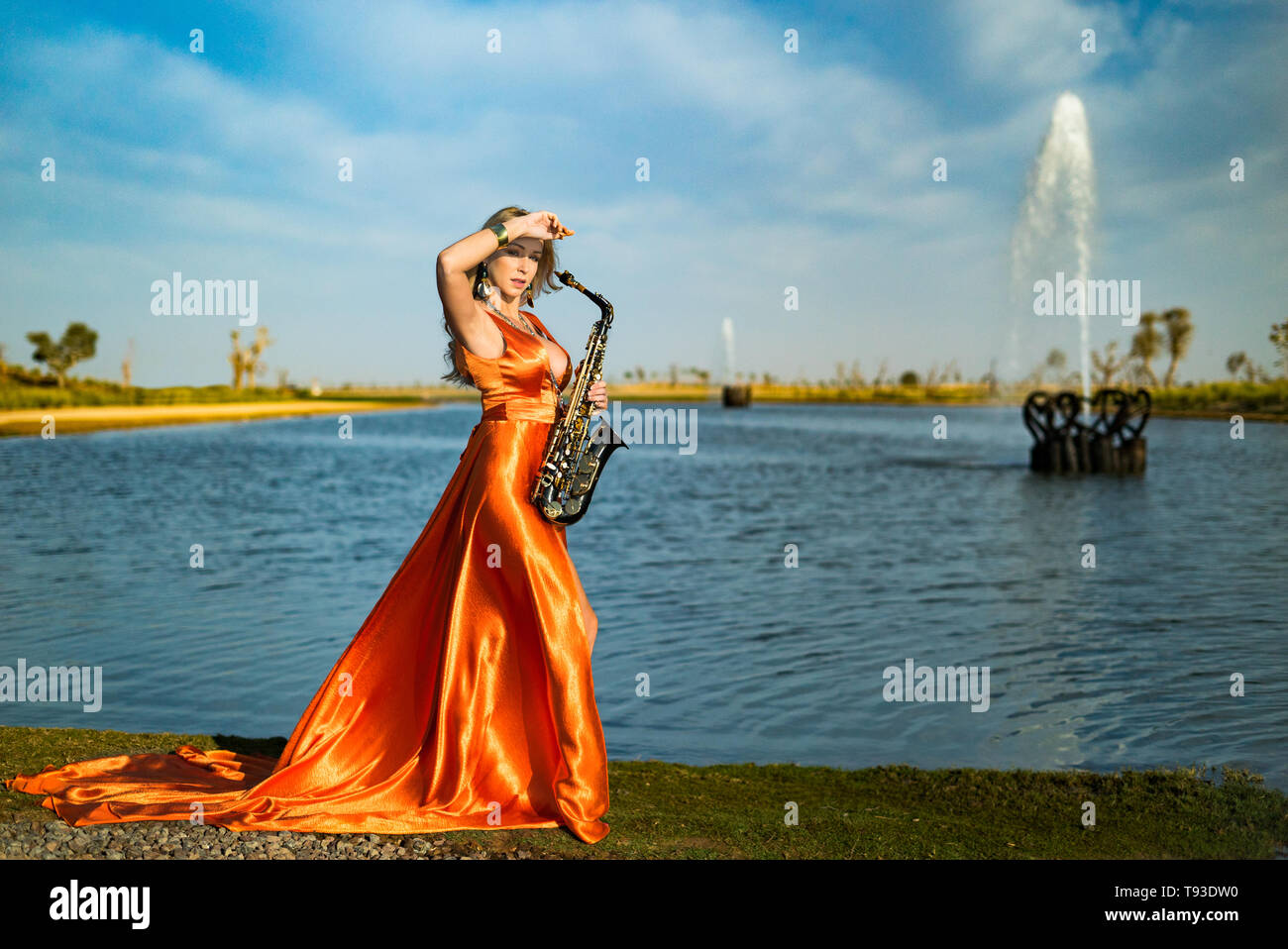 Mädchen mit sax lächelt, flirts. Gerne blonde Frau mit Big Bust spielt, führt auf goldy Saxophon in schönen Kleid Stockfoto