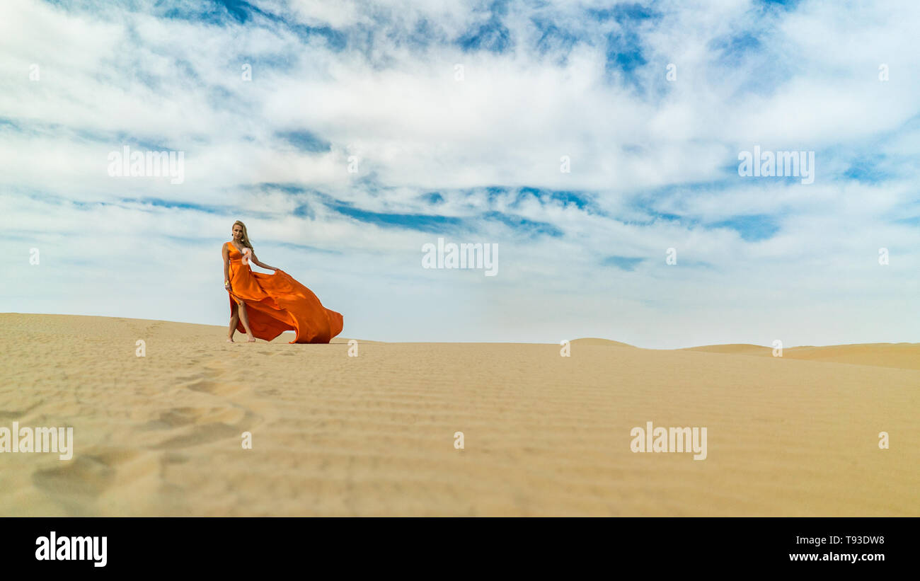 Mädchen Spaziergänge auf Wüste in Kleid flattern im Wind. Schöne Frau ist Wandern, Staing auf Sand oder Dune, berührt, zeigt ihre Beine. Blond sexy Dame in Stockfoto