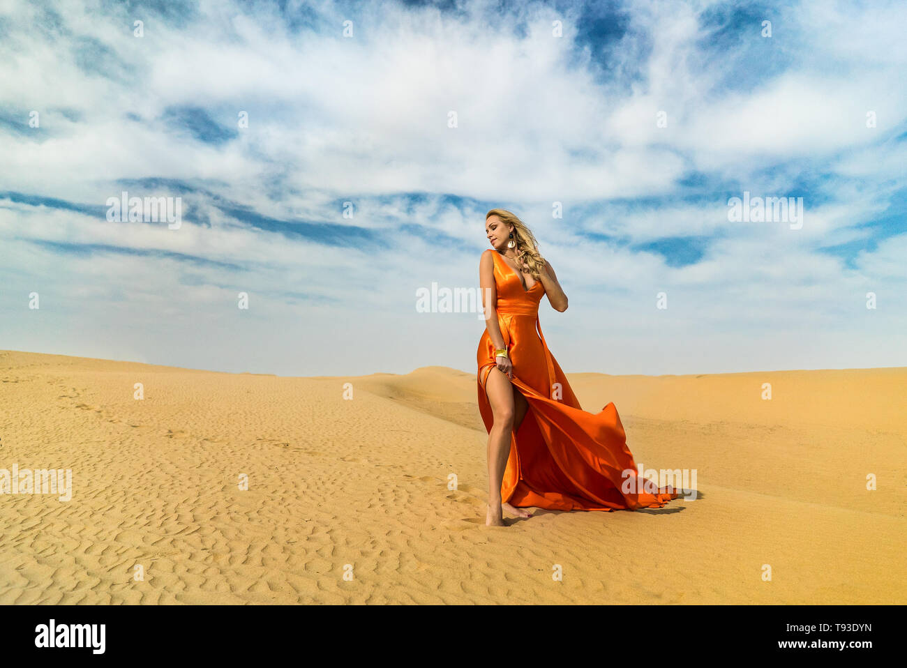 Mädchen Spaziergänge auf Wüste. Schöne Frau ist Wandern, Staing auf Sand oder Dune, berührt, zeigt ihre Beine. Blond sexy Lady in Kleid unter blauem Himmel Stockfoto