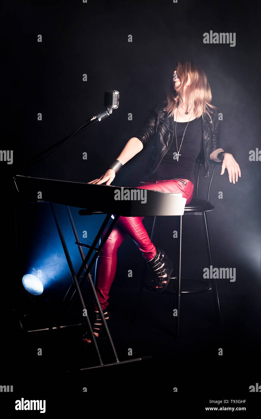 Blonde Mädchen Musiker Pianist spielt auf Digital Piano, sitzt auf einem Stuhl, singt zu retro Mikrofon. Frau Lehrerin zeigt, wie für die Wiedergabe von Musik Stockfoto