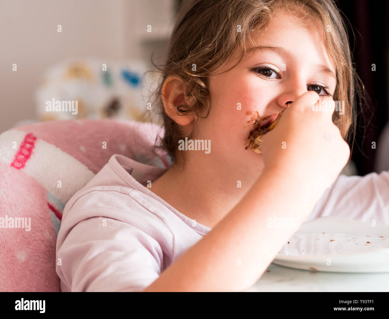 Kleine kaukasische Mädchen mit langen Haaren unordentlich Schokolade essen Stockfoto