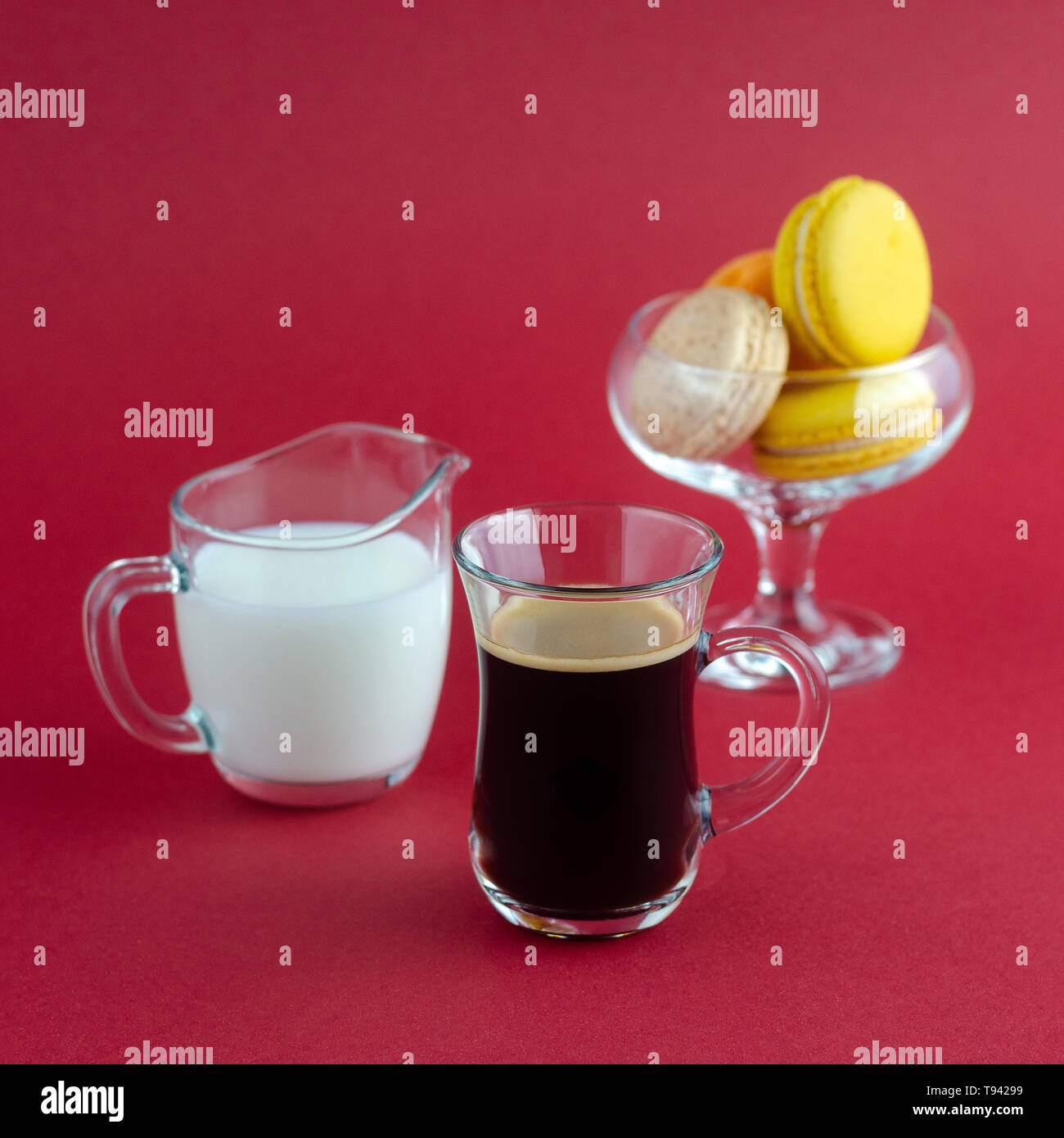 Eine transparente Tasse schwarzen Kaffee und einen Milchmann und eine Vase mit Cookies auf eine rote Fläche platziert Stockfoto