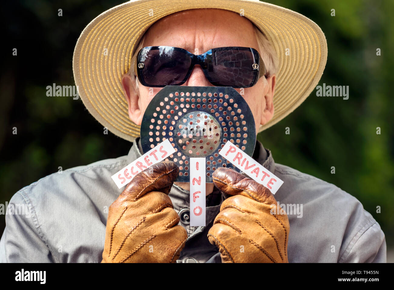 Parodie Konzept des Geheimagenten, Spy, mit dem Menschen in Panama Hut, Sonnenbrille und Handschuhe holding Sieb zu Mund mit Tags: Geheimnisse, Info und Privat. Stockfoto