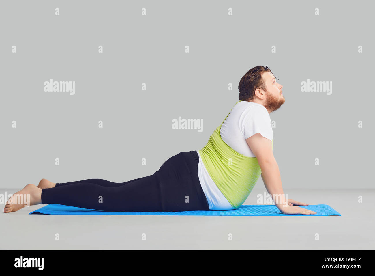 Eine lustige Fat Man tut Yoga Übungen auf einer Matte auf einem Hintergrund. Stockfoto