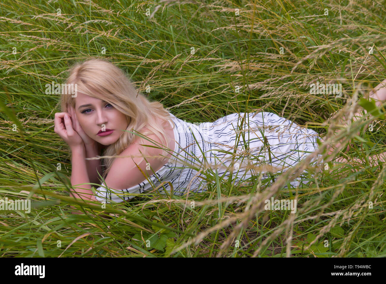 Verträumte junge blonde Frau entspannende liegen in einer Wiese mit hohem Gras Stockfoto