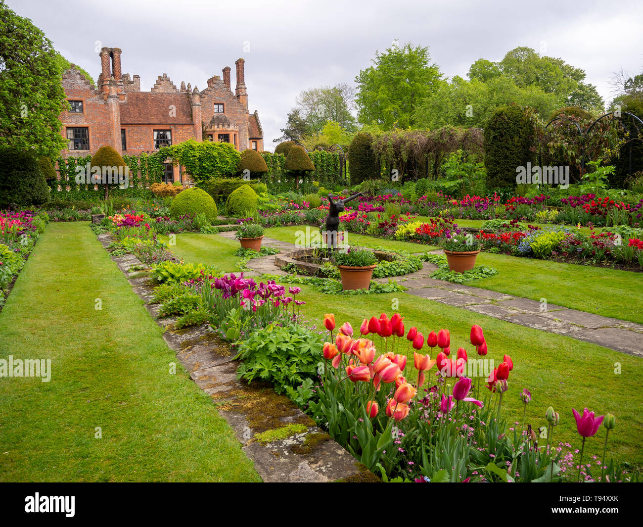 Chenies Herrenhaus und versunkenen Garten im Mai mit bunten tulip Sorten, Zierteich, Skulptur, Formgehölze, Gitter und frischen grünen Rasen.. Stockfoto