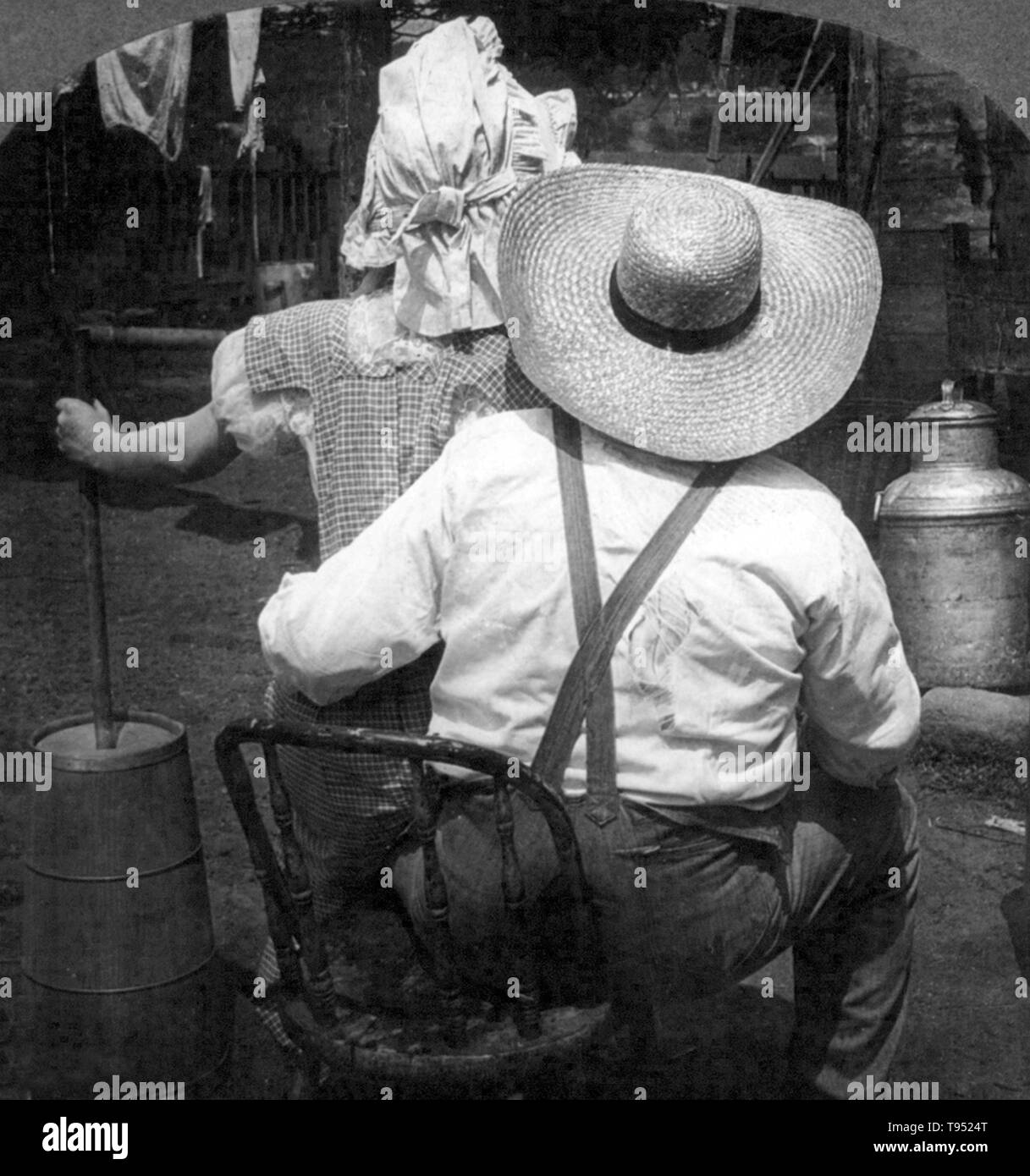 Mit dem Titel: "Butter überhaupt kommen?" zeigt eine Frau mit butterfass auf dem Schoß Mann sitzend; von hinten gesehen. 7/8 stereograph fotografiert von E.W. Kelley, 1906. Stockfoto