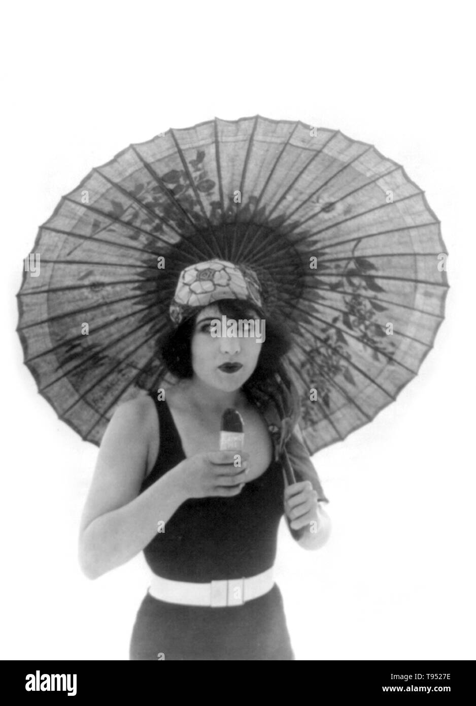 Titel: "Betty Compson mit Sonnenschirm, in Badehose, Blick leicht nach rechts, essen Eskimo Pie." Betty Compson (März 19, 1897 - April 18, 1974) war ein US-amerikanischer Schauspieler und Filmproduzent. Die meisten berühmten in Stummfilmen und frühen Tonfilms, ist sie am besten in ihre Performances in den Docks von New York und von Barker, Letztere verdienen eine Nominierung für den Academy Award für die beste Schauspielerin bekannt. Ihre Popularität erlaubte ihr kreative Kontrolle über Ihre Filme zu haben, wie sie auch in der Lage war, zu produzieren. Stockfoto