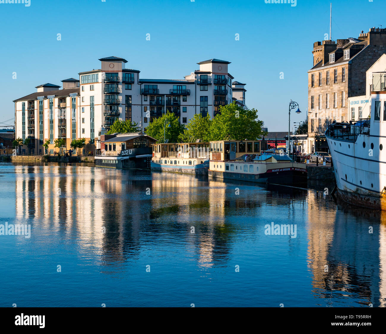 Leith Docks, Edinburgh, Schottland, Großbritannien, 16. Mai 2019. UK Wetter: ein sonniger Tag geht zu Ende über den Hafen in Leith mit Gebäuden und Lastkähne auf dem Ufer von den letzten Strahlen der Sonne spiegelt sich im Wasser des Leith Fluss lit Stockfoto