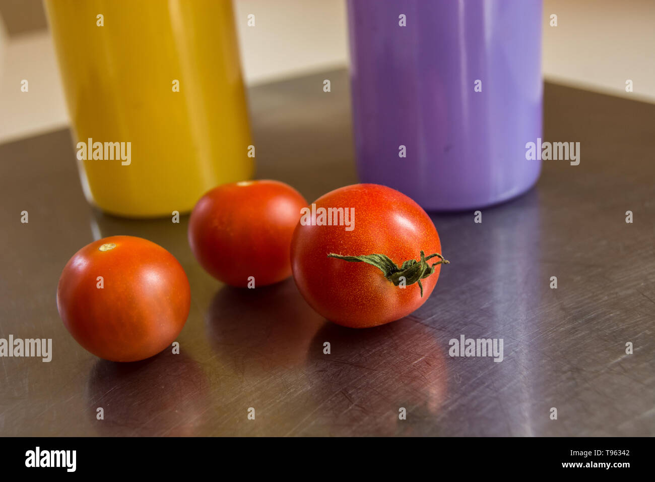 Drei kleine Tomaten liegen auf einem Aluminium Zähler und bunten Glas Geschirr Stockfoto