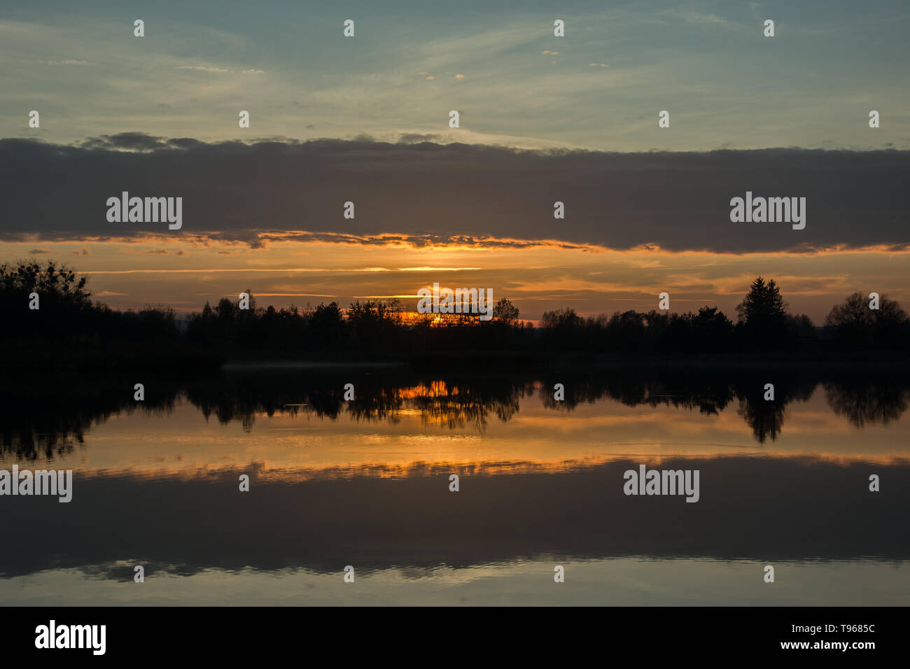 Sonnenuntergang auf dem See, Bäume am Ufer und Reflexion von Cloud im Wasser Stockfoto