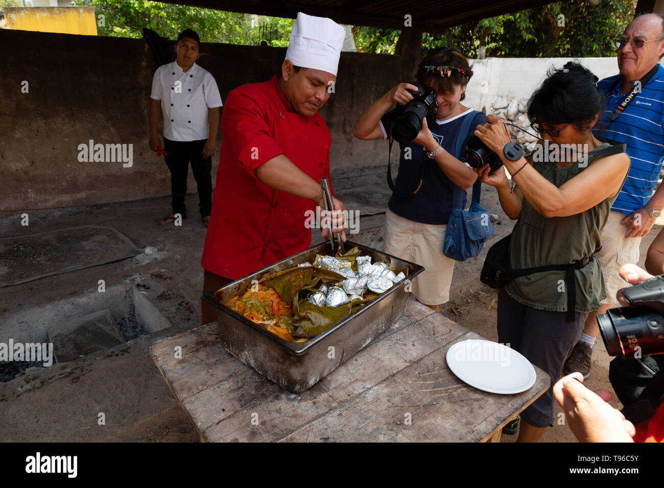 Mexiko essen - Touristen beobachten ein Koch entfernt Essen in einem unterirdischen Ofen (Erde Backofen), Campeche, Yucatán, Mexiko Lateinamerika gekocht Stockfoto