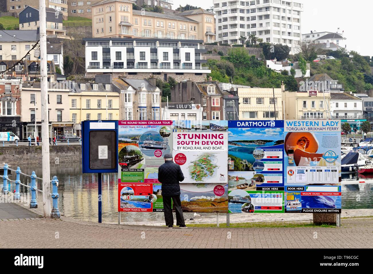 Rückansicht eines älteren Mannes an einem bunten Aushang in Torquay Werbung Touristen reisen auf verschiedene Verkehrsmittel, Devon, England Stockfoto