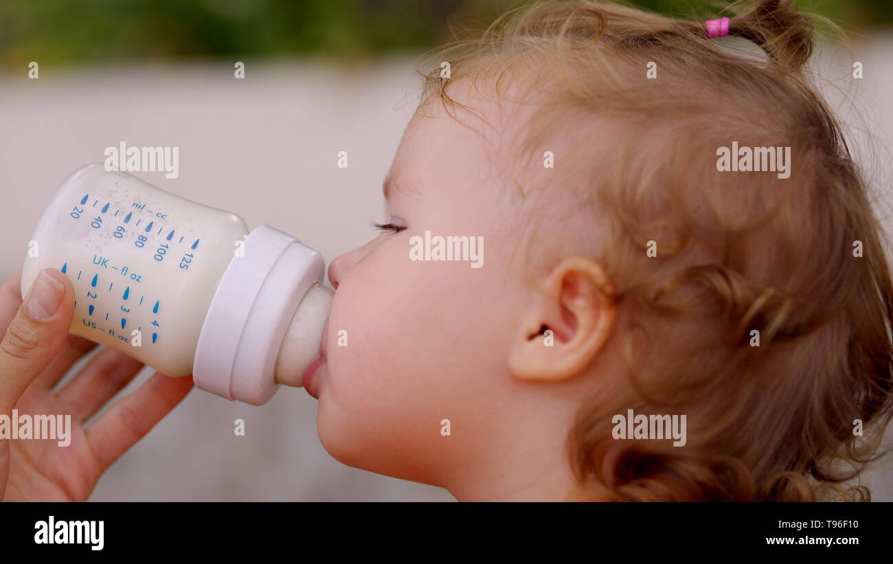 Wenig schöne Mädchen mit blauen Augen trinkt Milch aus der Flasche. Das  Kind hält die Flasche selbst Stockfotografie - Alamy