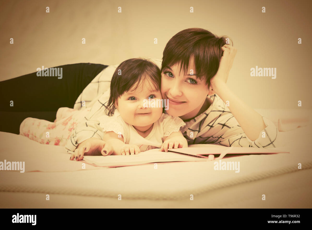Glückliche junge Mutter und Baby Mädchen das Lesen eines Buches auf dem Bett Stockfoto