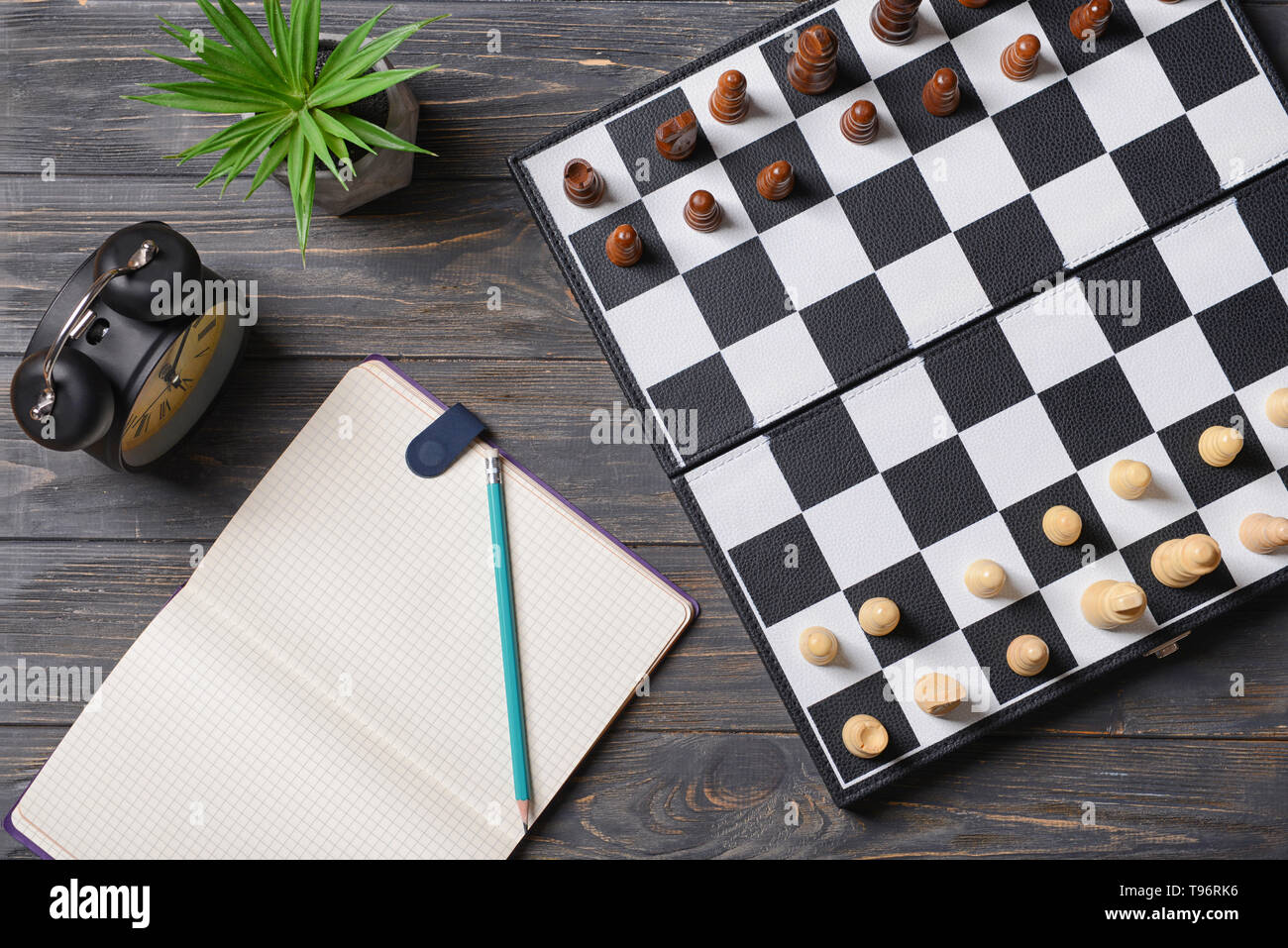 Schachfiguren mit Spielbrett und Wecker auf hölzernen Tisch Stockfoto