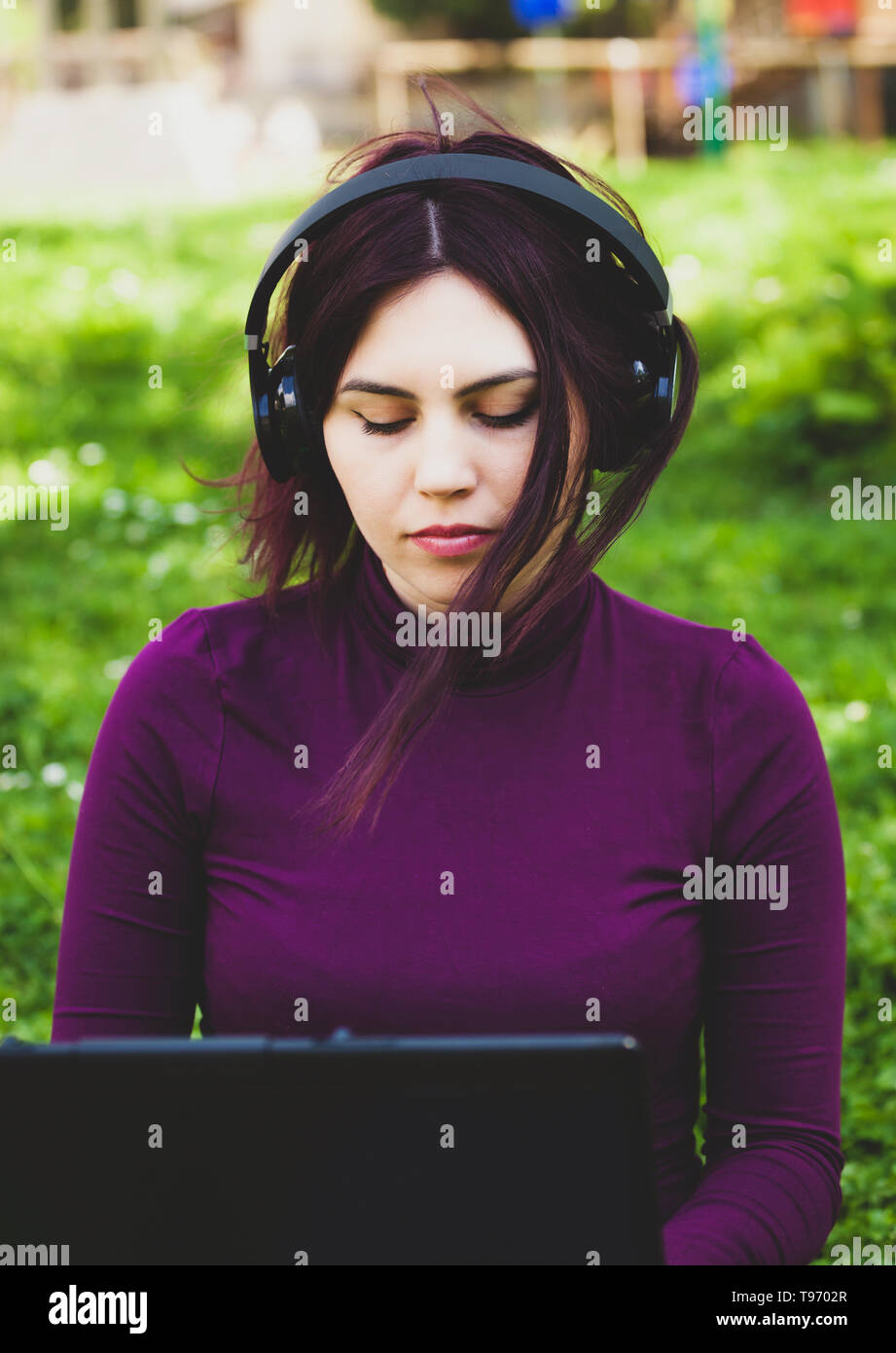 Schöne junge hübsche Frau im Park im Freien mit Laptop Computer Musik hören. Stockfoto