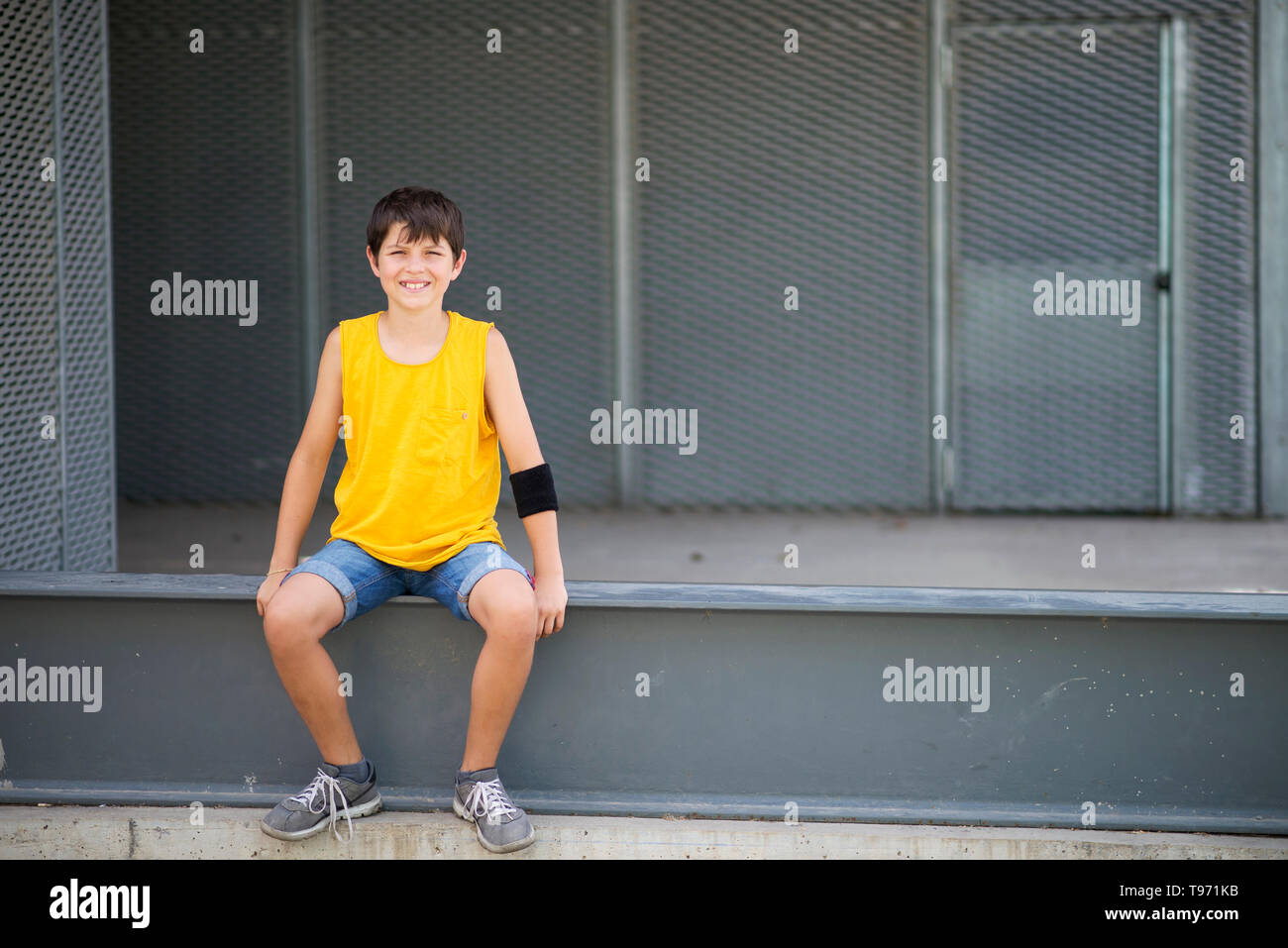 Vorderansicht der lächelnde Junge sitzt auf einem metallischen Zaun, während Sie die Kamera an einem hellen Tag Stockfoto