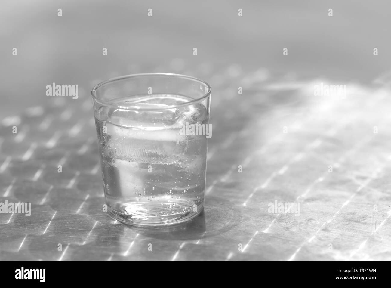 Glas Wasser mit Eis auf einem metallischen Tisch im Freien an einem hellen Tag Stockfoto