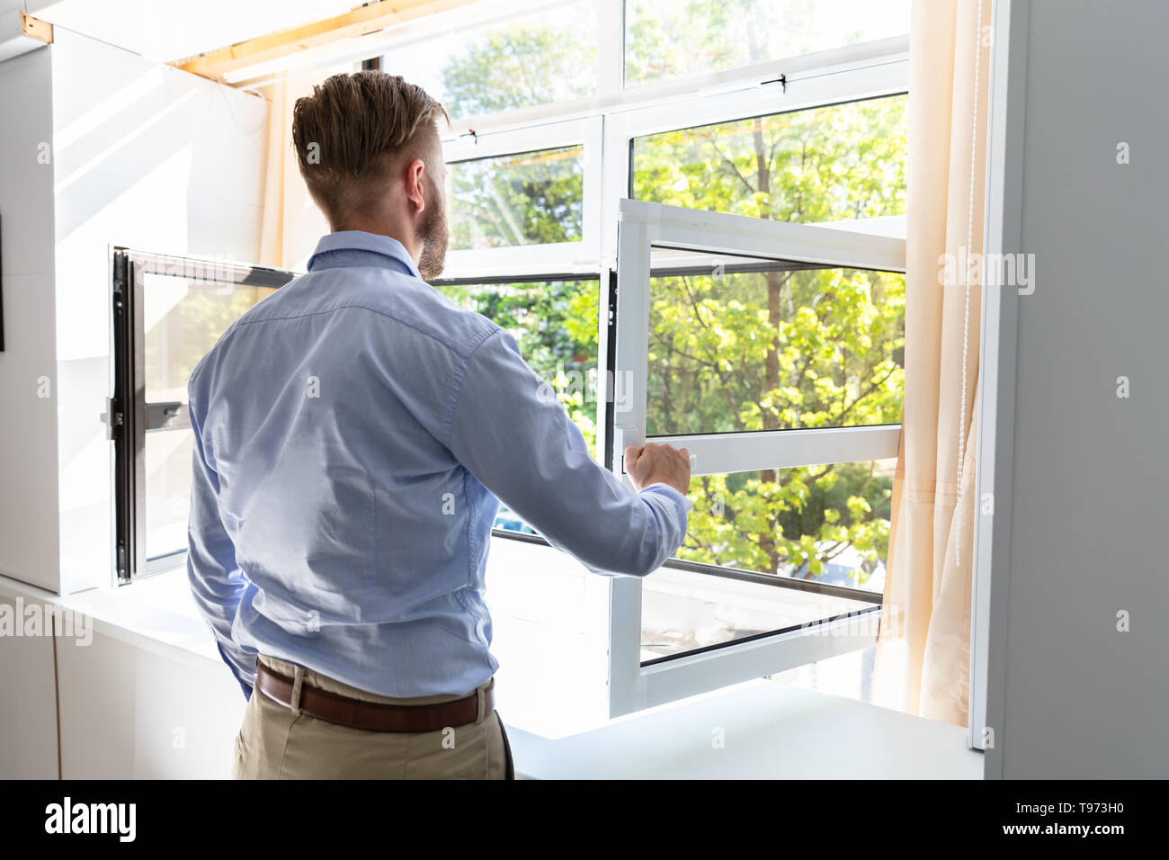 Ansicht von hinten von einem Mann öffnen Fenster, um frische Luft zu Hause Stockfoto