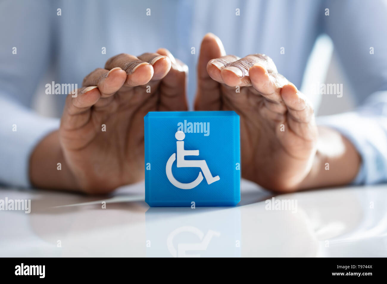 Nahaufnahme eines menschlichen schützende Hand blau Cubic Block mit Behinderten Handicap Symbol Stockfoto