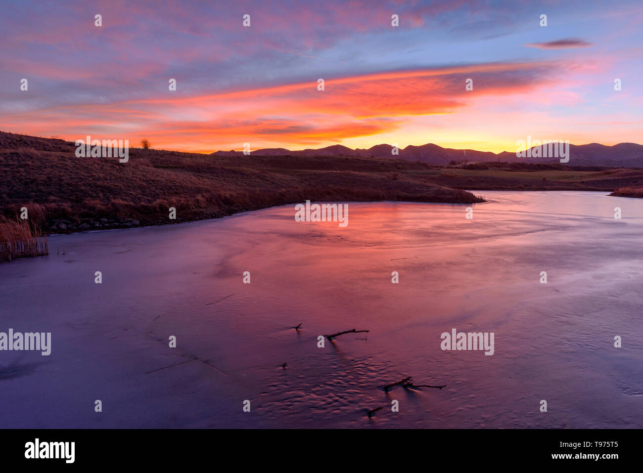 Letzten Sonnenlicht - Die Wolken sind leuchtend rote von der letzten Sonnenlicht über einen gefrorenen Bergsee. Bear Creek Park, Denver-Lakewood, Colorado, USA. Stockfoto