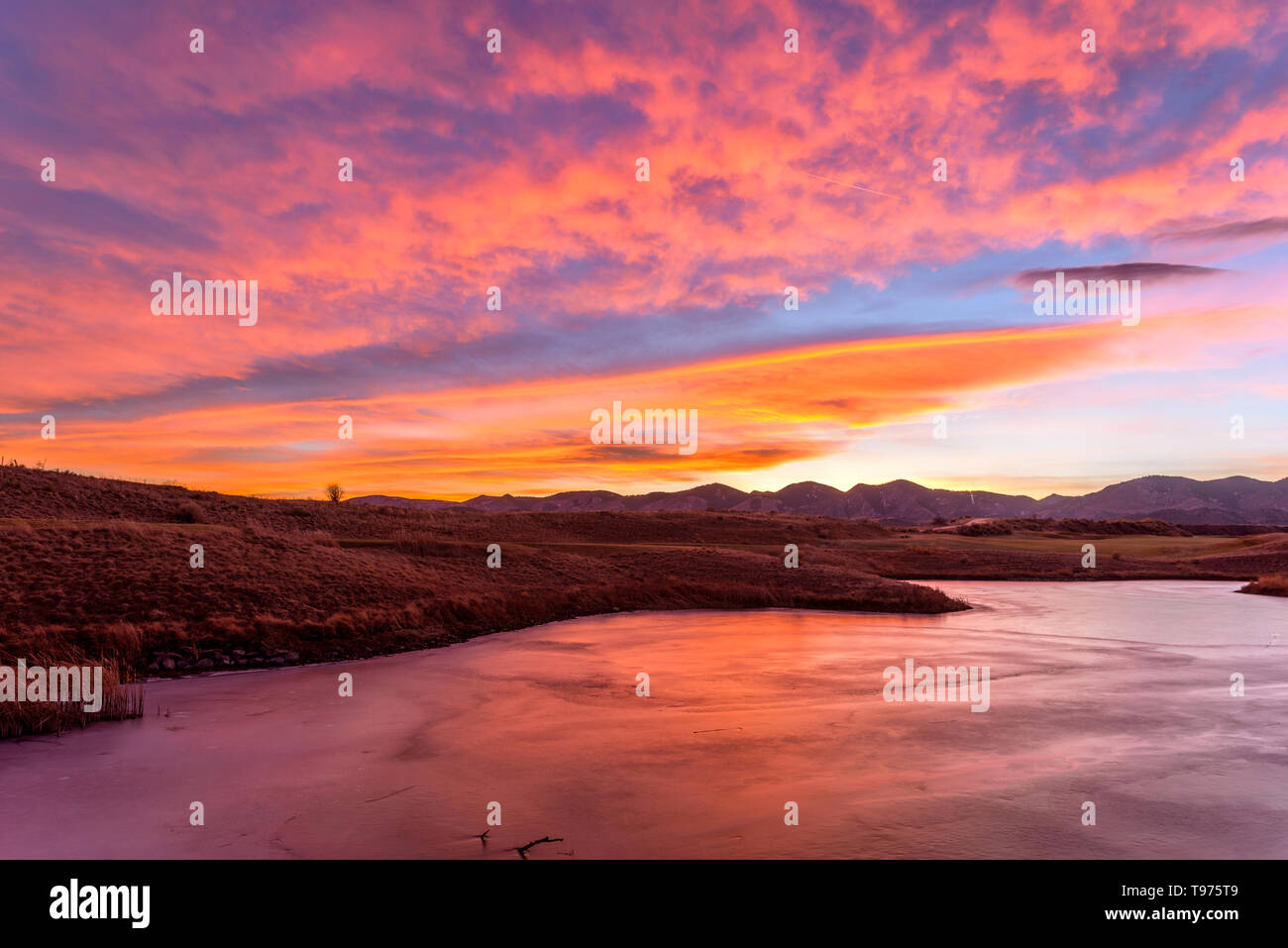 Brennender Himmel über einen zugefrorenen See - leuchtend roten Sonnenuntergang Himmel über einen gefrorenen Bergsee. Bear Creek Park, Denver-Lakewood, Colorado, USA. Stockfoto