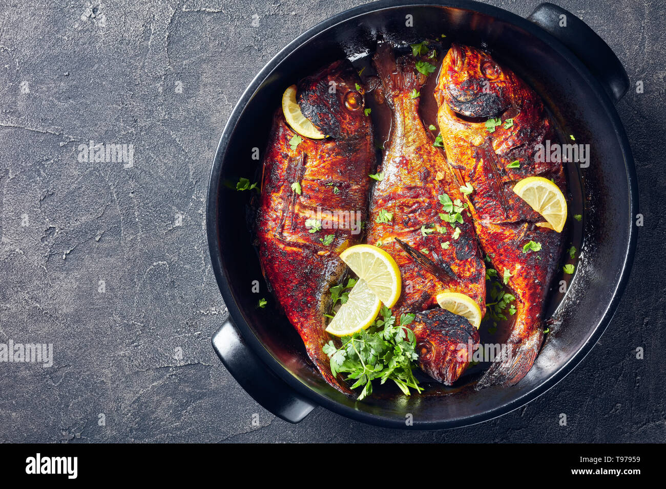 Köstliche frisch gebratenen dorado Fisch mit Zitronenscheiben in einer schwarzen Keramik Auflaufform auf einer konkreten Tabelle, Ansicht von oben, Kopieren, flatlay Stockfoto