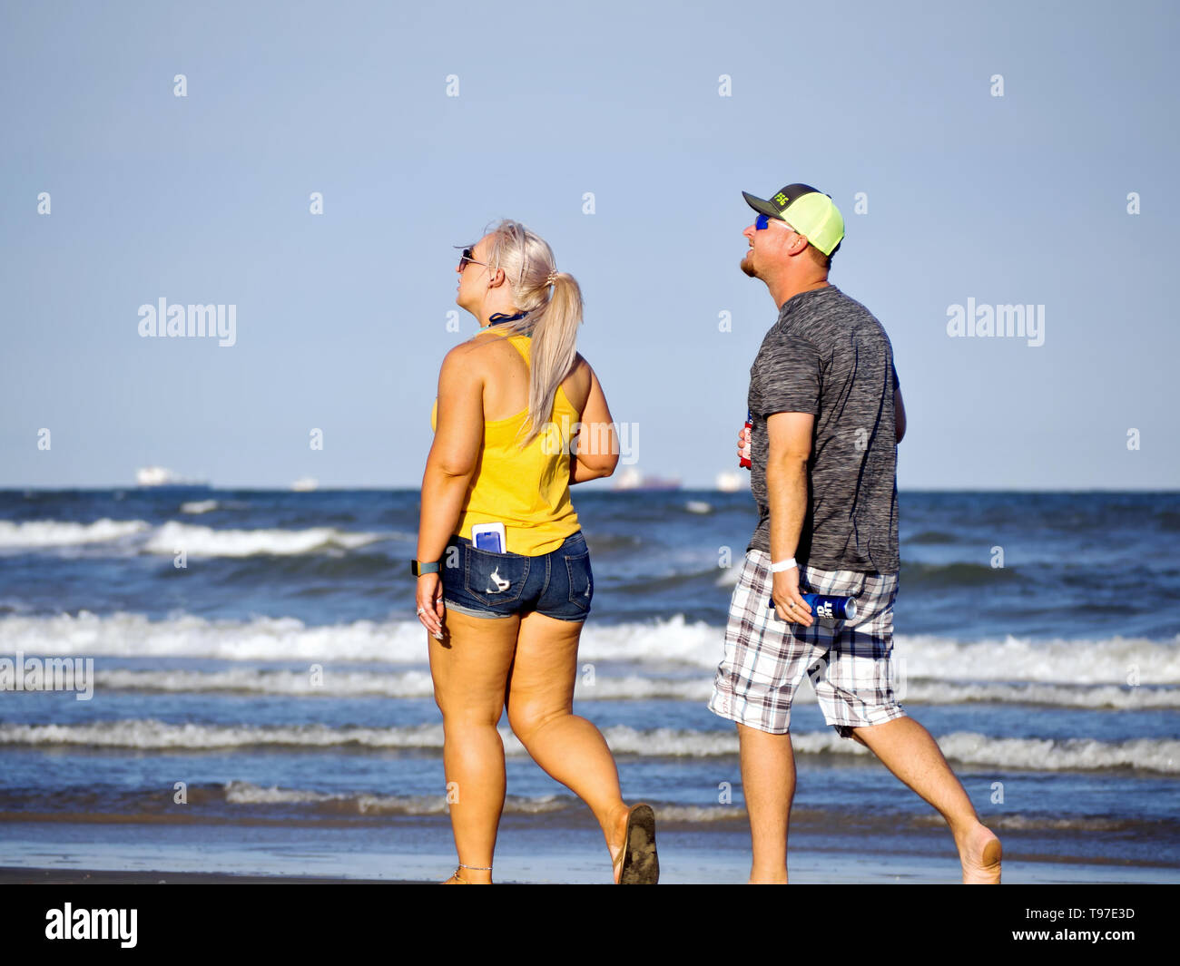 Kaukasische Mann und Frau bis in den Himmel schauen, als sie neben dem Golf von Mexiko am Strand in Port Aransas, Texas USA schlendern. Stockfoto