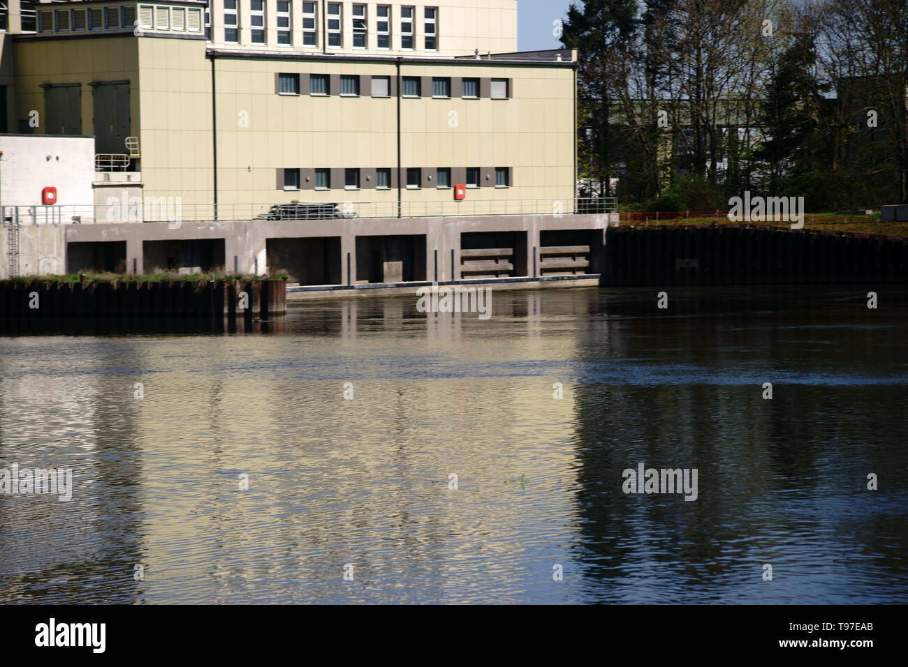 Ein Wehr mit industriellen Gebäuden und einem wasserwerk am Ufer eines Flusses. Stockfoto