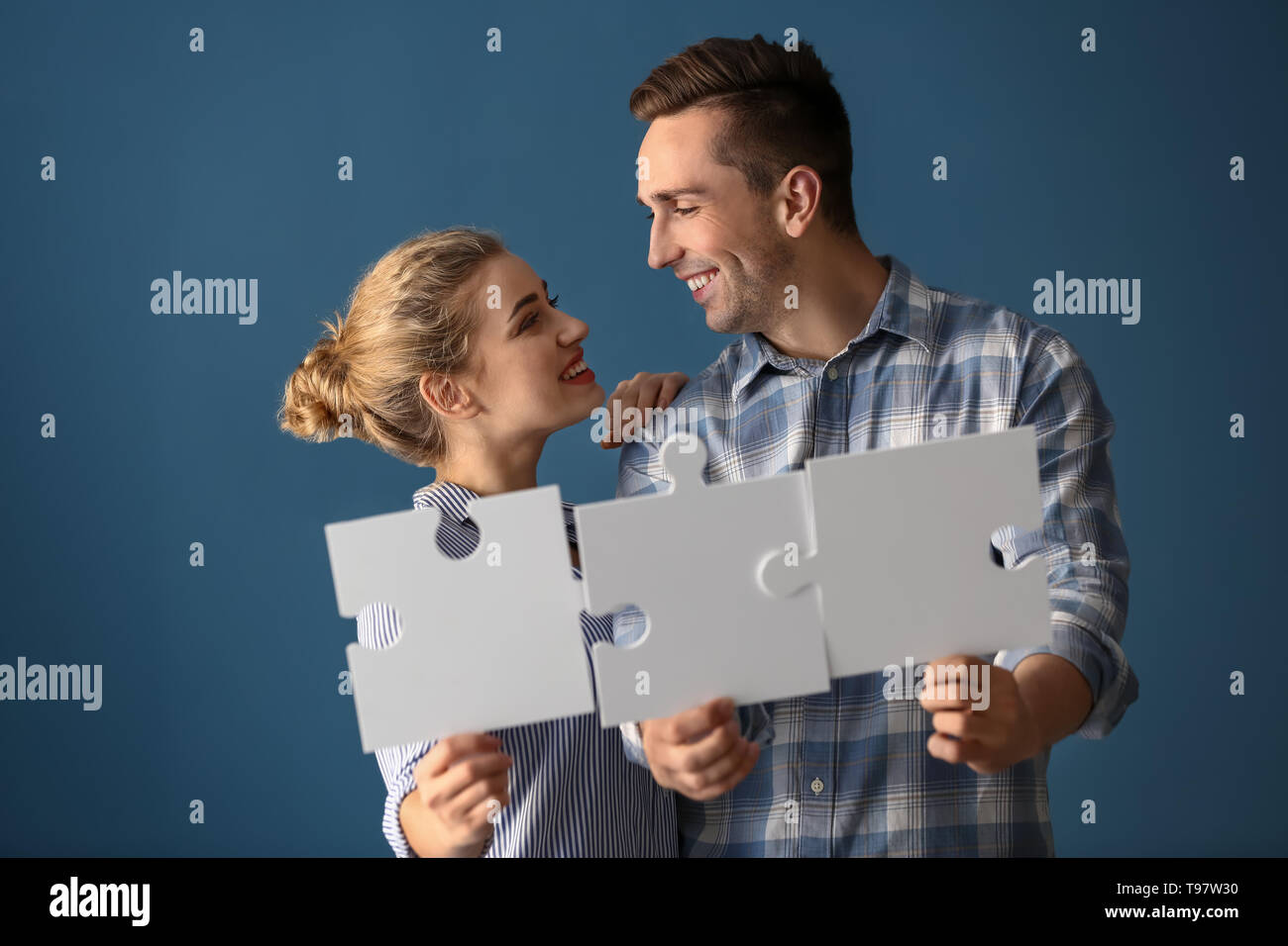 Junges Paar mit Stücken von Puzzle auf farbigen Hintergrund Stockfoto