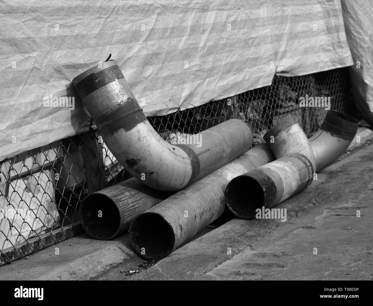 Nahaufnahme von beschädigten Rohren aus Metall auf Betonboden, Monochrom Stockfoto