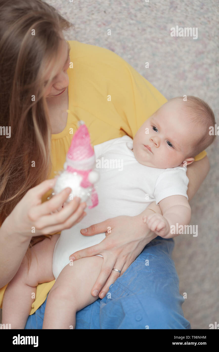 Ein Baby in den Armen eines langhaarigen Frau an einem Spielzeug in der Hand suchen Stockfoto