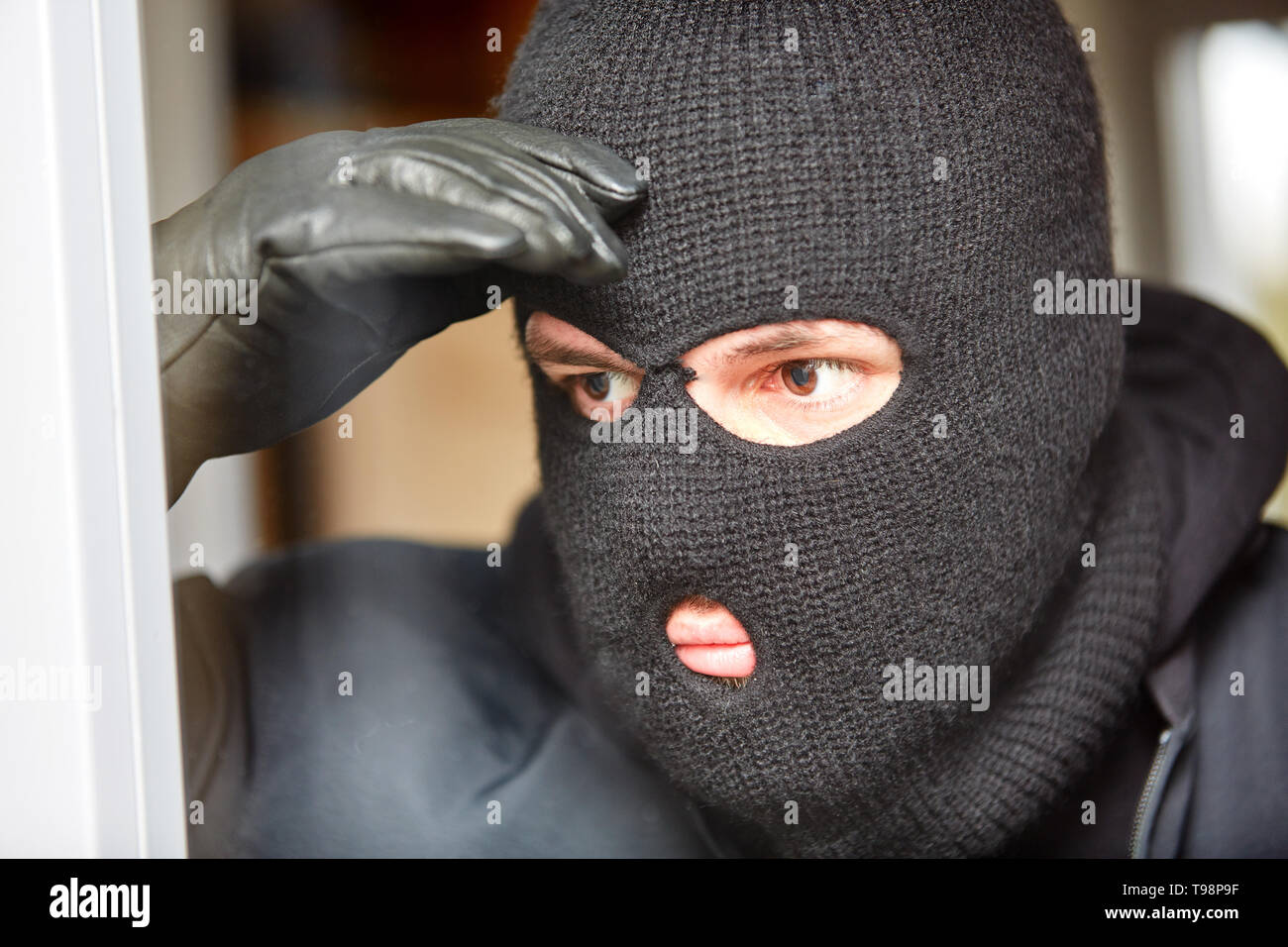 Maskierte Einbrecher mit Balaclava späht durch das Fenster eines Hauses vor einem Einbruch Stockfoto