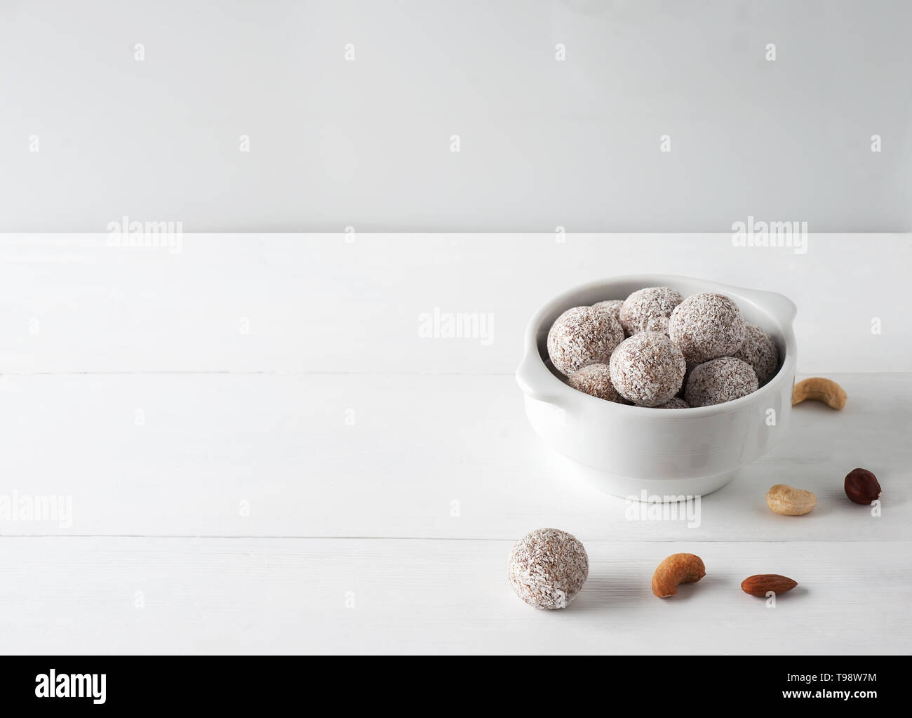 Vegane Spezialitäten. Bild der gesunde Energie Kugeln mit Nüssen, Kokosnüsse, Chips und trockene Früchte. Weiße Platte auf dem weißen Holz- Hintergrund. Selektive konzentrieren. Stockfoto