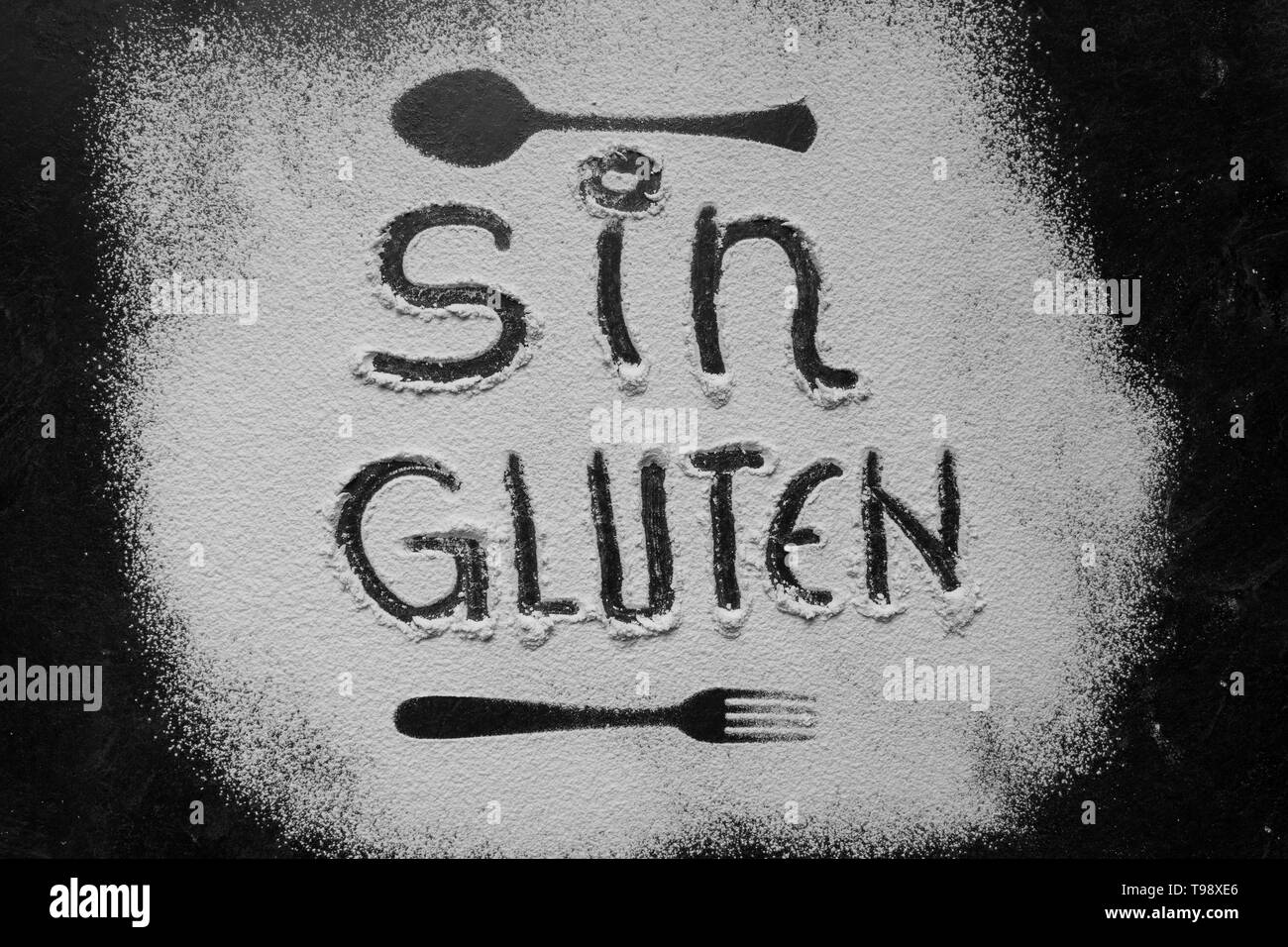 Glutenfreies Mehl mit Text Glutenfrei in spanischer Sprache mit Löffel und Gabel Silhouette mit Mehl auf dunklem Hintergrund Textur, die Horizontale v Stockfoto