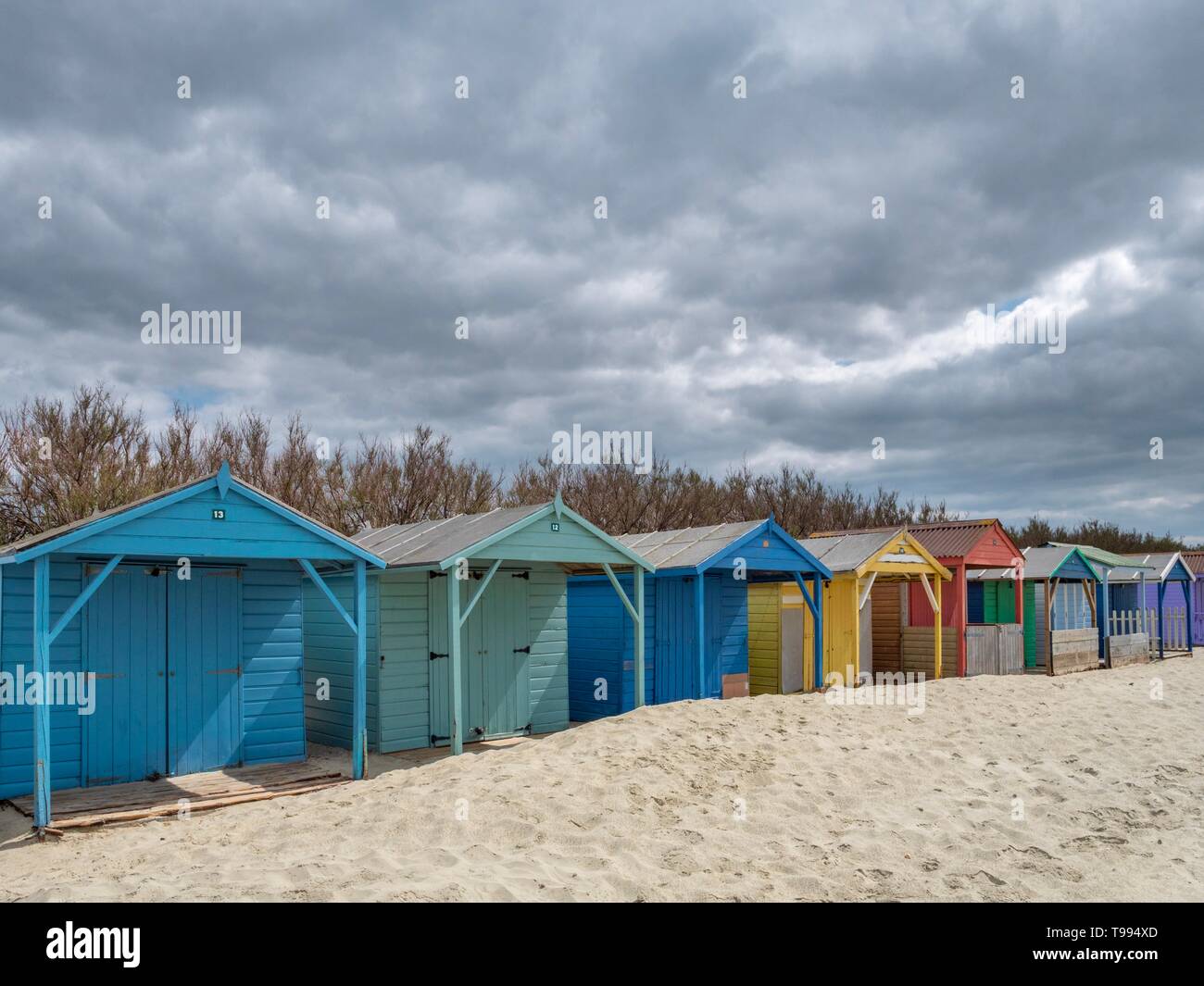 Eine Reihe von bunten hölzernen Umkleidekabinen am Strand an einem Sandstrand im Süden von England an einem bewölkten Tag Stockfoto