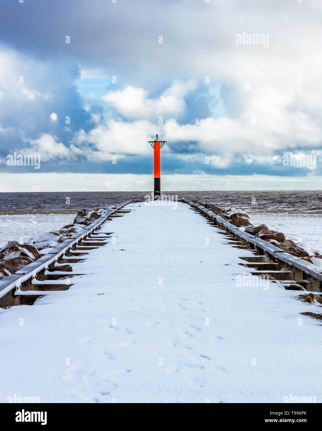 Orange Rundumleuchte auf einem schneebedeckten Wellenbrecher in der Ostsee, Lettland. Stockfoto