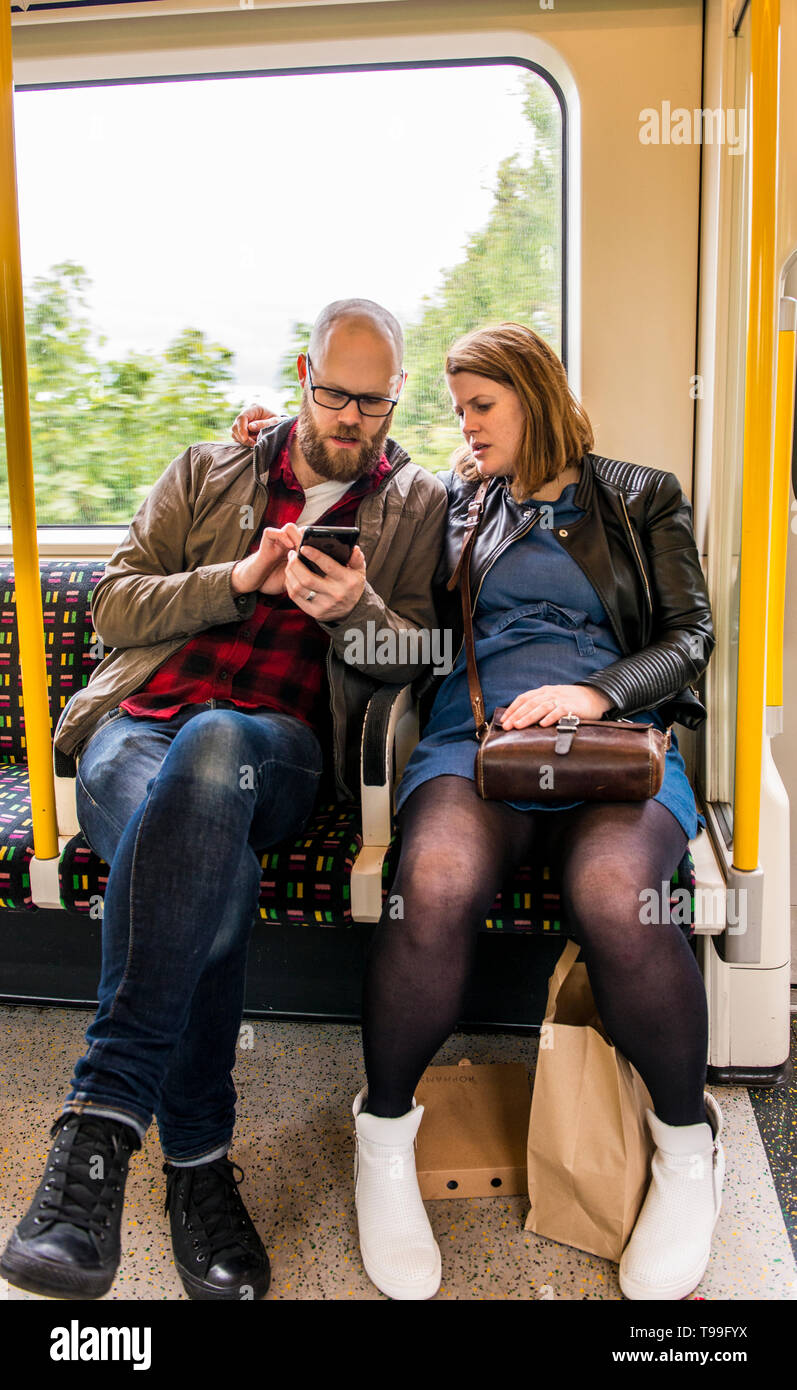 Heterosexuelle Paare auf U-Bahn, zusammen zu sitzen, bei der man das Smartphone suchen Stockfoto