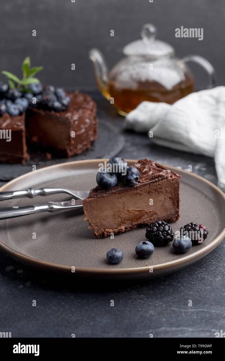 Stück Schokolade Kuchen mit ganzen Kuchen hinter Teekanne mit Tee auf dunkelgrauem Hintergrund und. Konzept der süßen essen kann. Stockfoto