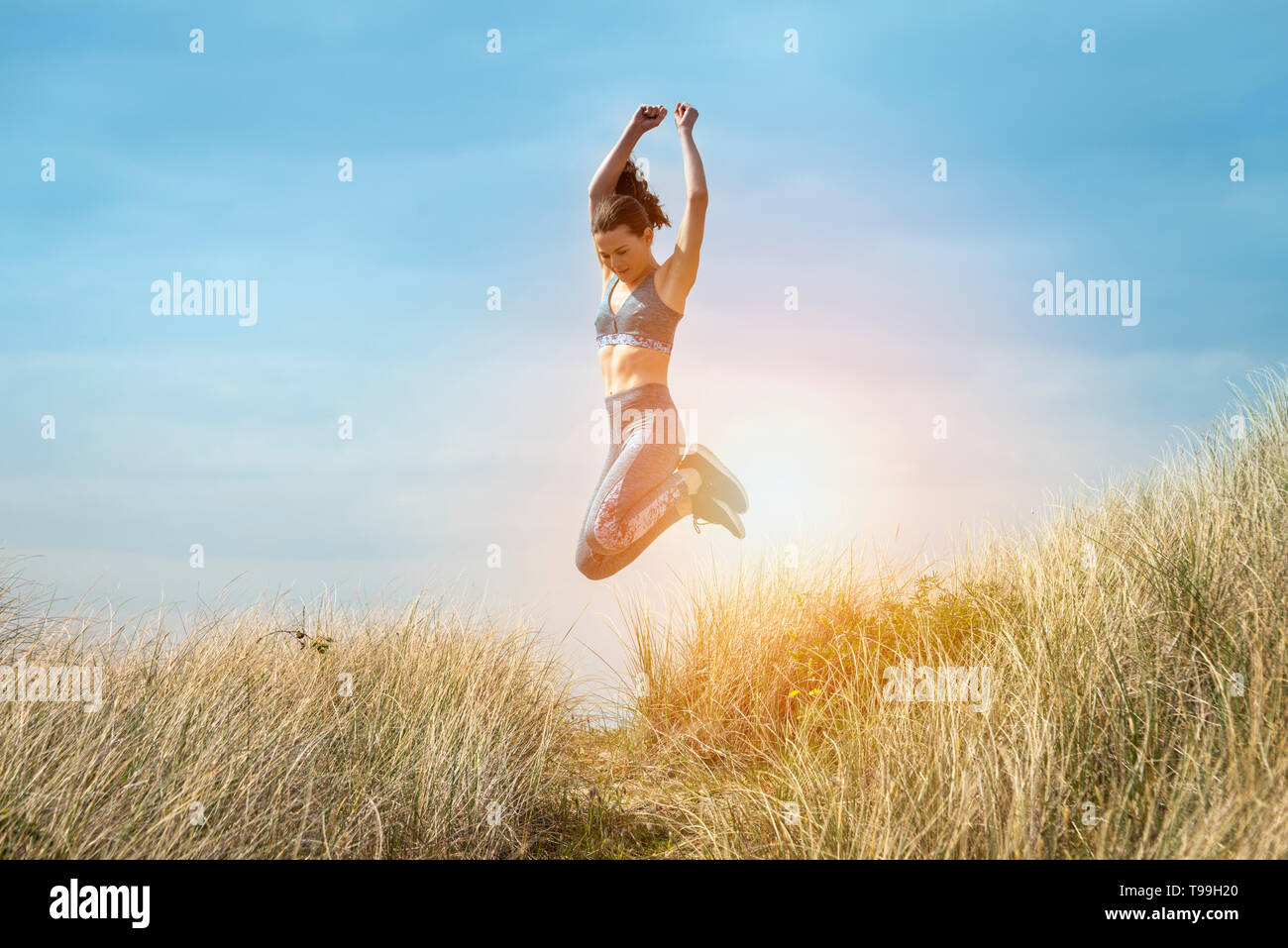 Sportliche Frau laufen und springen in den Sanddünen, gesund und glücklich, springen vor Freude. Stockfoto
