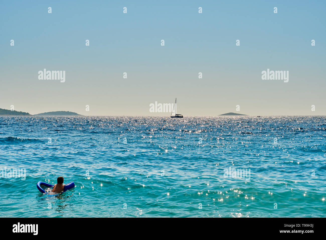 Man schwimmt auf Luftmatratze, auf dem Segelboot in der Ferne in Sibenik, Dalmatien, Kroatien Suche Stockfoto
