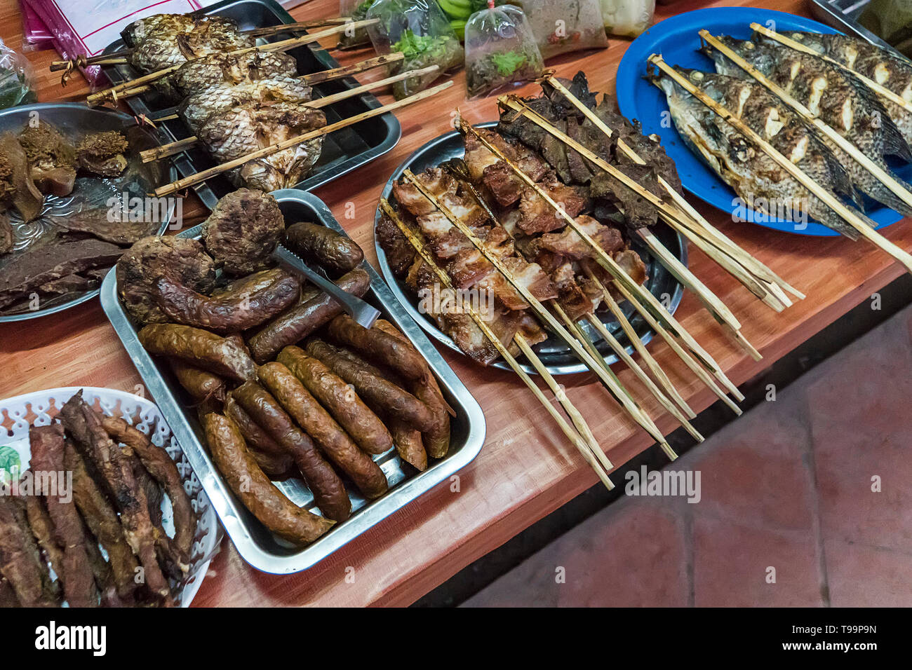 Straße Nahrungsmittel in Laos, ausgewählte konzentrieren, Grill. Verschiedene Arten von Fisch, Fleisch und andere Lebensmittel auf den Zähler auf dem Tisch. Street Food in Asien. Stockfoto