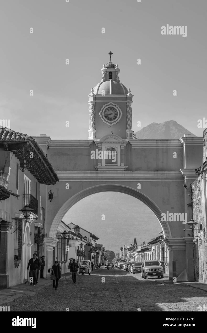 Arco de Santa Catalina, historischen Gebäude aus Stein, Menschen zu Fuß und das Agua Vulkan im Hintergrund, an einem sonnigen Tag, in Antigua, Guatemala Stockfoto