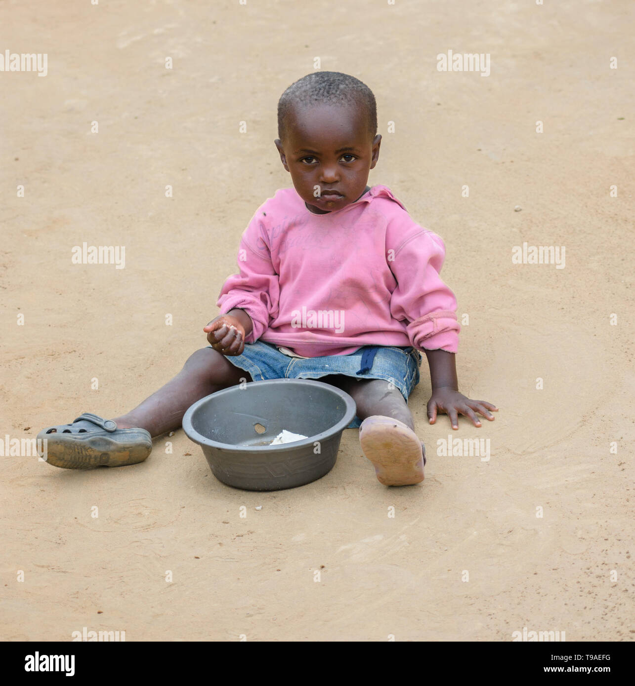 Eine malawische Kind sitzt auf dem Boden nsima aus einem Kunststoff Schüssel in einem Dorf in Dedza Malawi zu essen Stockfoto