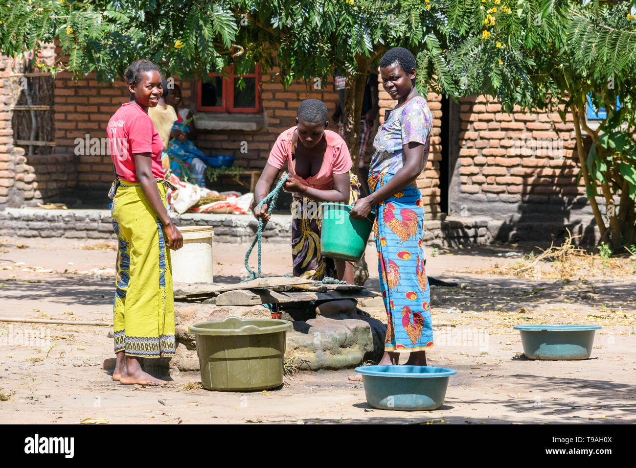 Malawische Frauen Zeichnung Wasser in der Mittagssonne aus einem flachen Brunnen in einem Dorf mit Plastikeimer und Seil Stockfoto
