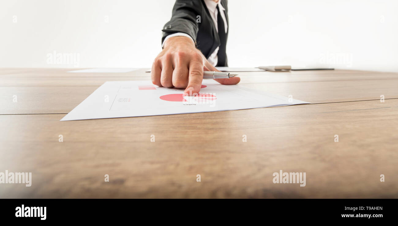 Niedrigen Winkel Weitwinkelaufnahme mit rückläufigen Perspektive eines Geschäftsmannes auf eine analytische Kreisdiagramm auf einen Schreibtisch aus Holz mit dem Finger zeigen. Stockfoto