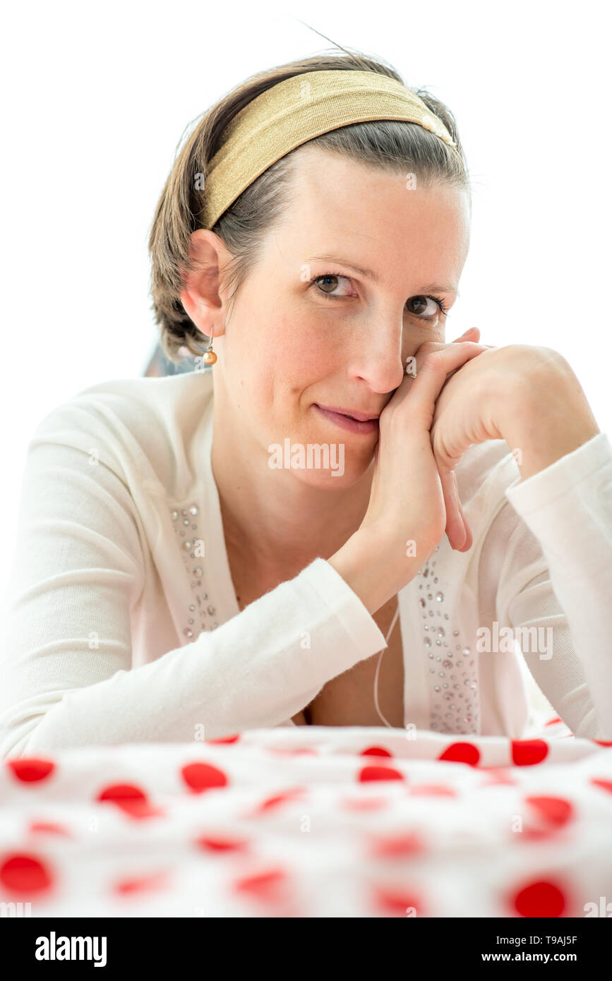 Freundlich attraktiven charismatischen jungen Frau liegen auf einem roten und weißen Tupfen Bett in die Kamera schaut mit einem schelmischen Lächeln. Stockfoto