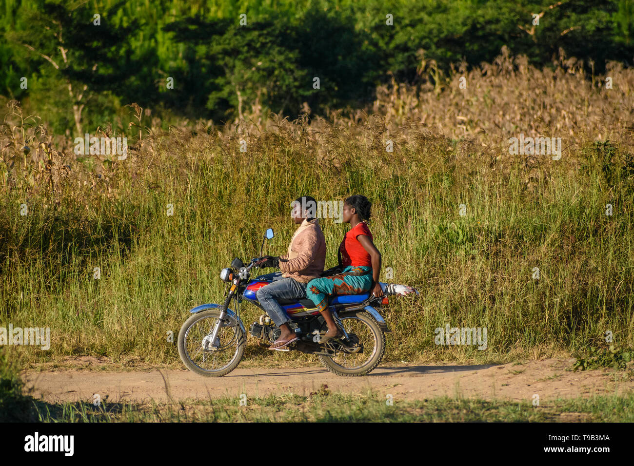 Malawian man reitet ein Motorrad auf einem Feldweg mit einem Malawischen Frau Reiten als Passagier Stockfoto