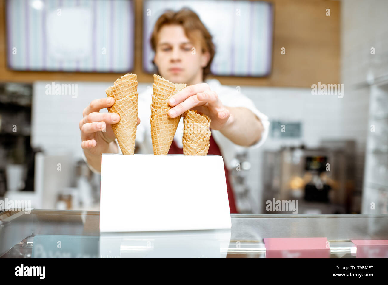 Stattliche Verkäufer unter Waffel Kegel während Eis für den Client in der modernen Konditorei Stockfoto